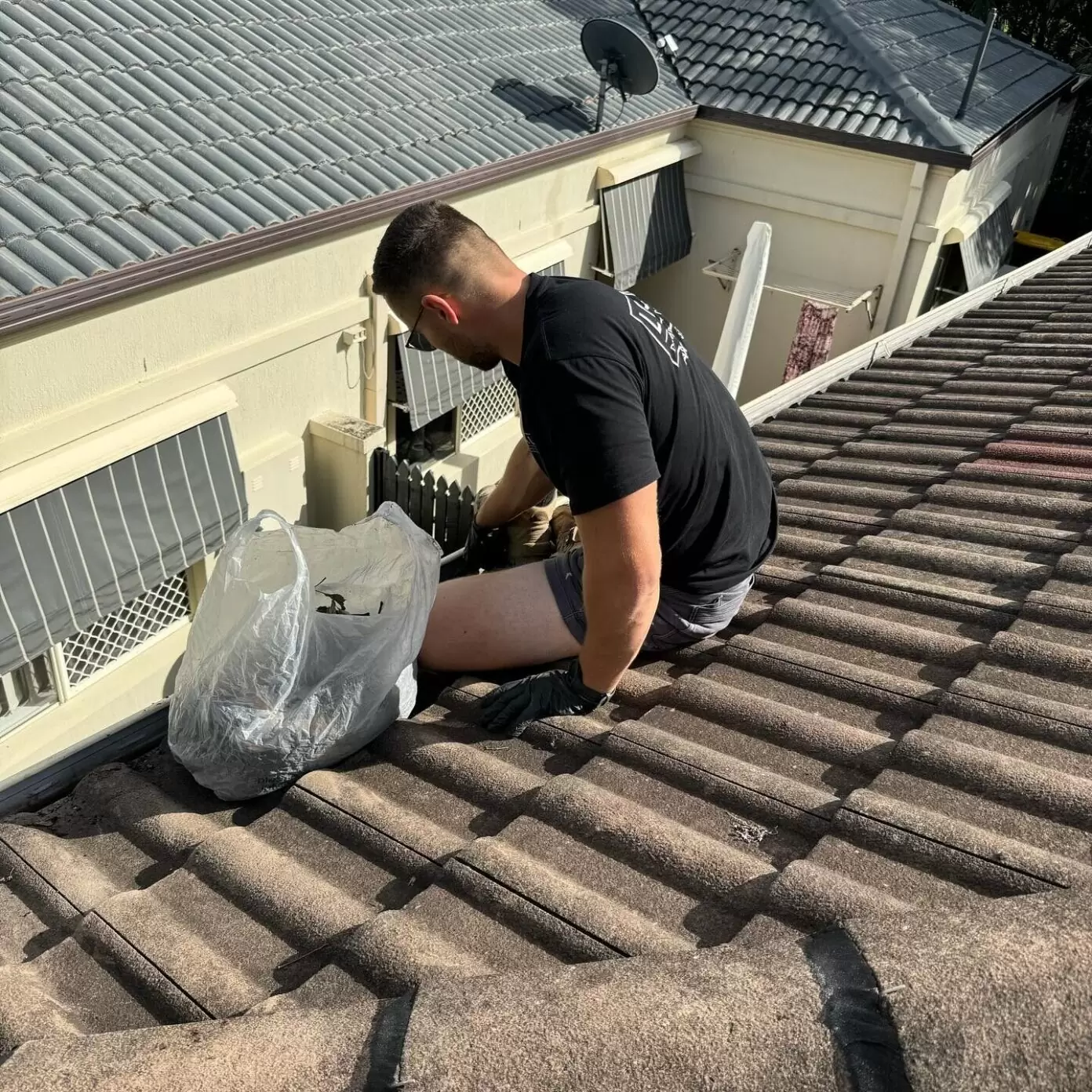 Plumber cleaning roof gutters on a residential property in preparation for storm season