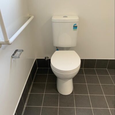 Standard toilet suite installed in an accessible bathroom with grab rails and black tile floor