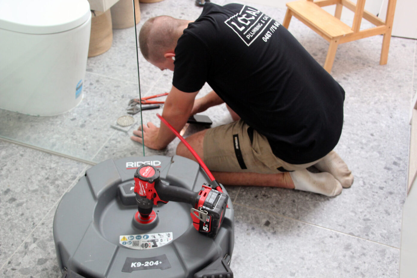 Gold Coast residential plumber using a drain cleaning machine on a bathroom floor waste