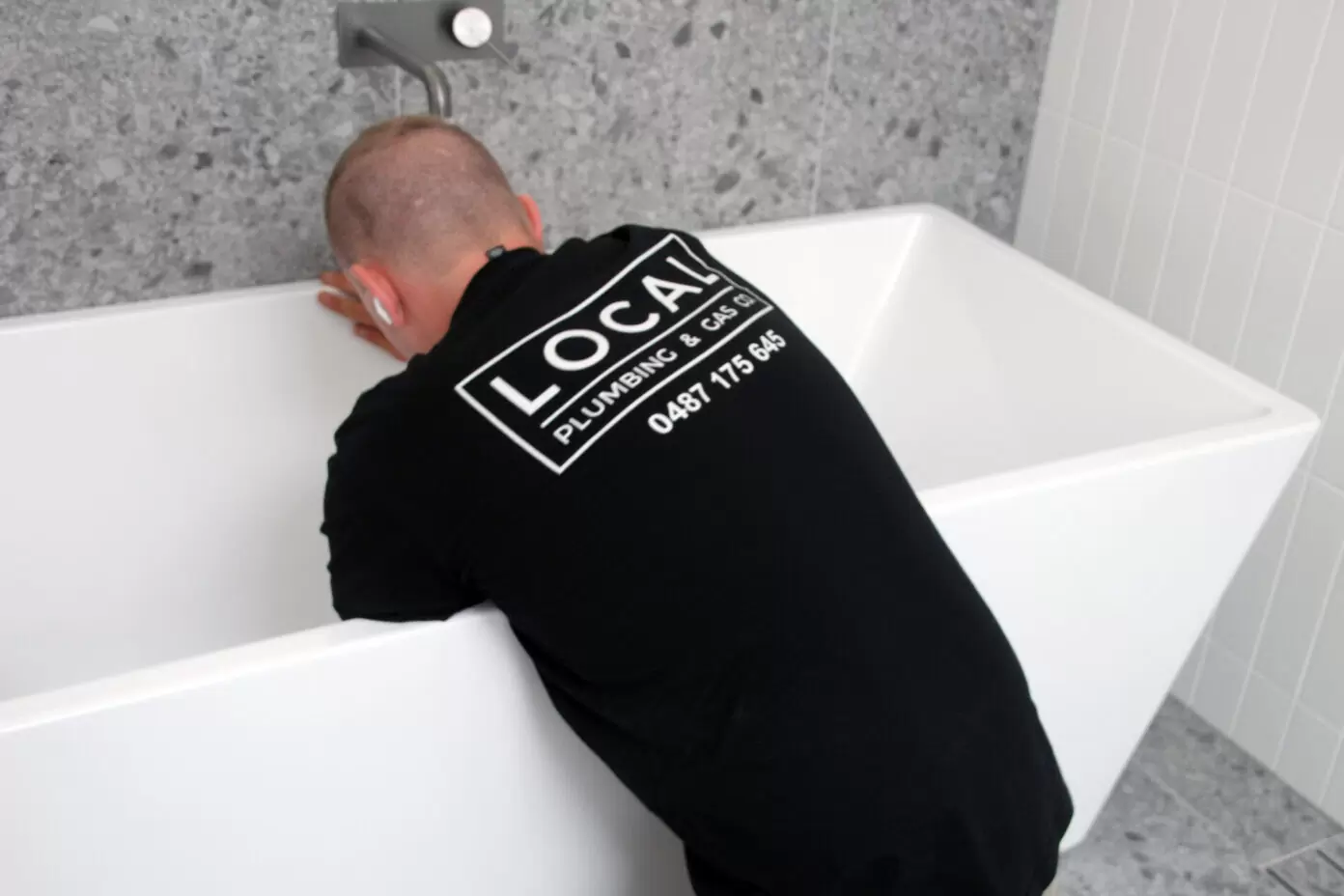 Licensed plumber installing freestanding bathtub in a modern Gold Coast bathroom