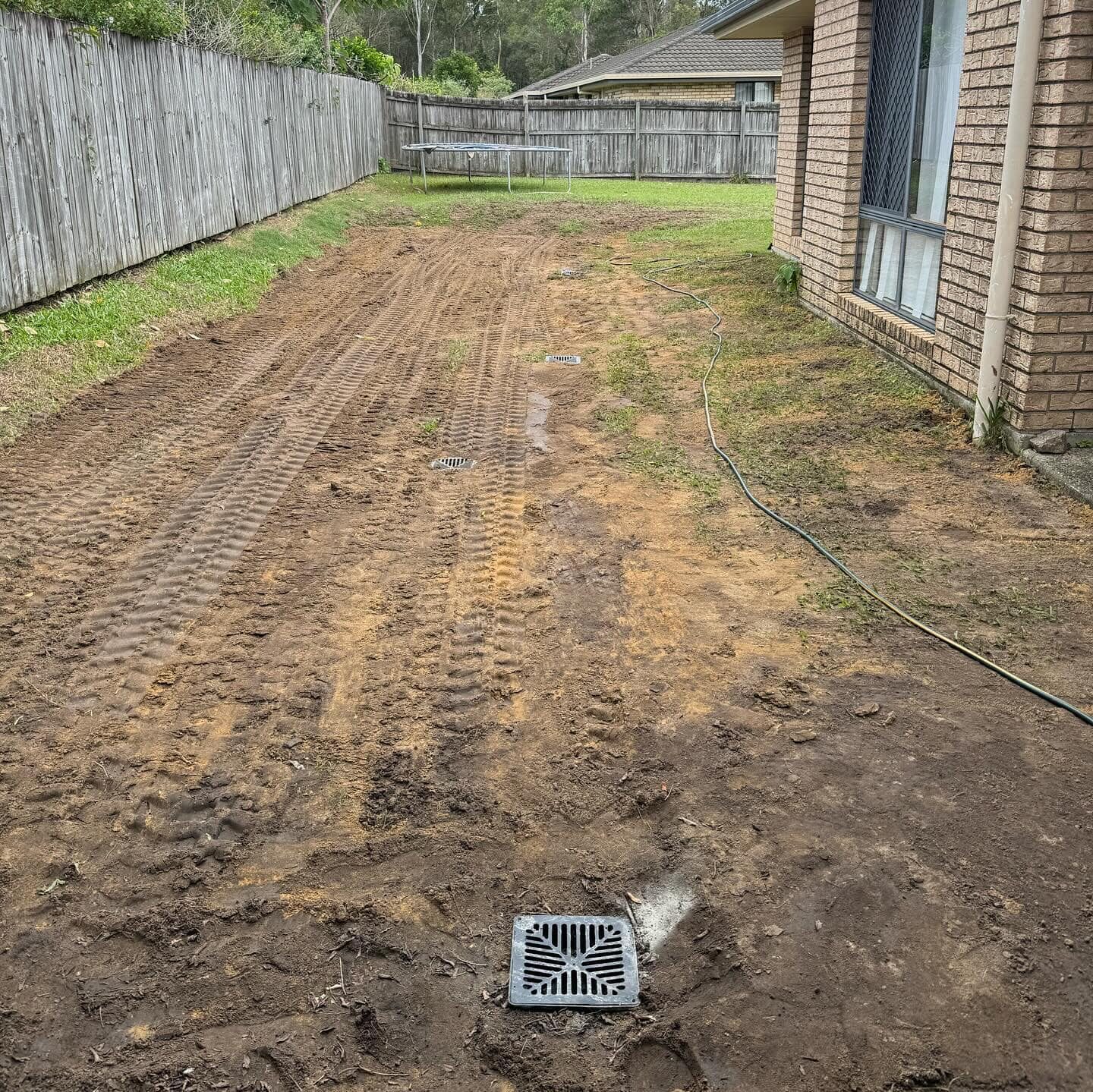 Completed stormwater drainage installation beside a brick house in Morayfield, showing new yard grates and levelled soil.