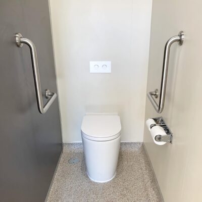 Wall-facing school toilet installation with dual flush button and grab rails in Brisbane primary school