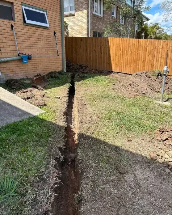 Narrow stormwater trench freshly dug beside home after drainage system failure in Brisbane.