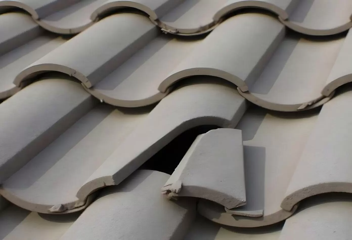 Close-up of a cracked and dislodged roof tile exposing a gap underneath—an early warning sign that roof replacement may be needed.