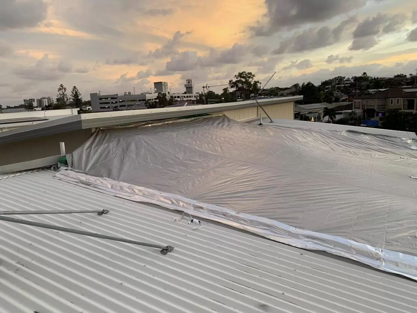 Temporary emergency tarp installed on a metal roof in Gold Coast at sunset, protecting a residential property from further water damage.