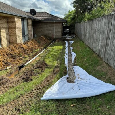 French drain installation in progress at a Morayfield property, with geofabric lining and gravel along the fence line.