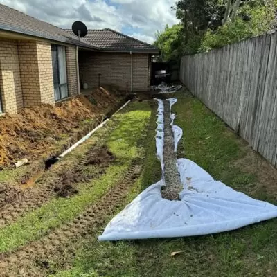 French drain installation in progress at a Morayfield property, with geofabric lining and gravel along the fence line.