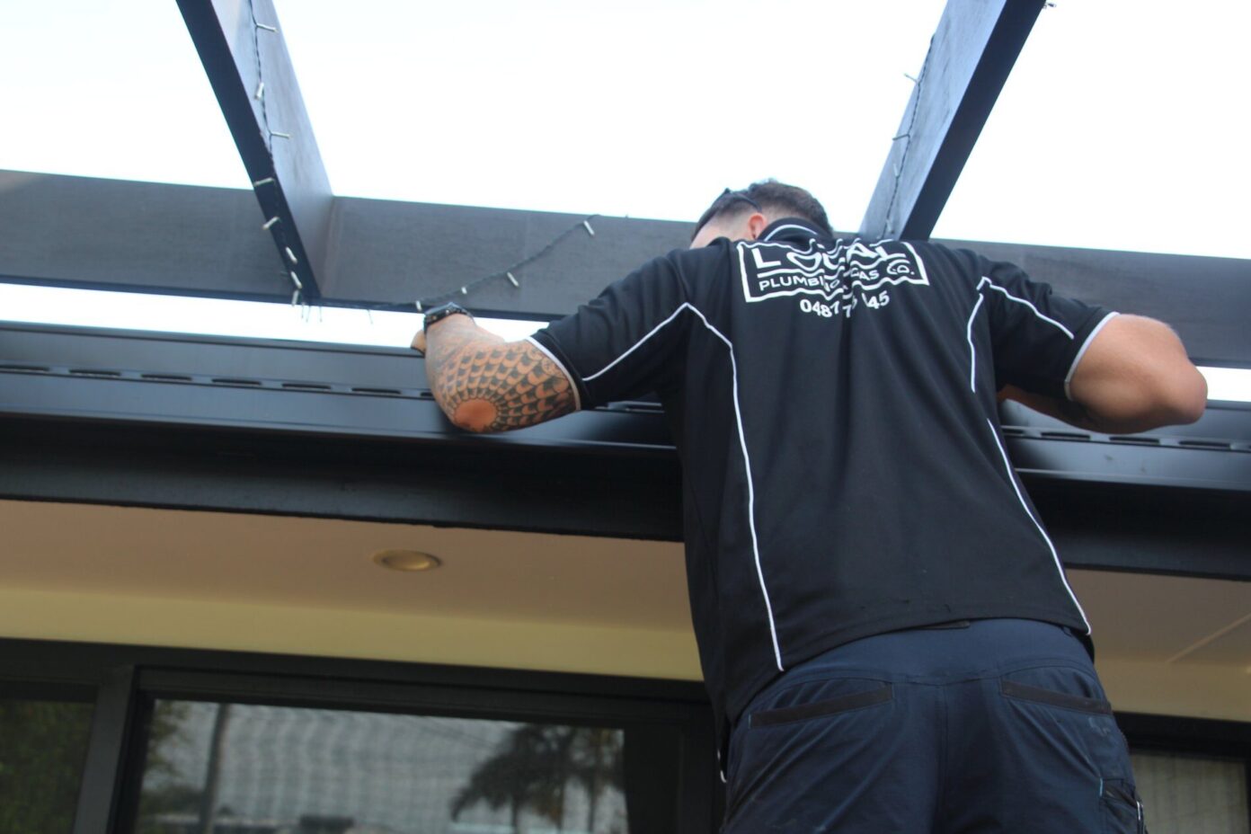 Plumber inspecting roof gutters for blockages and drainage issues at a Gold Coast property