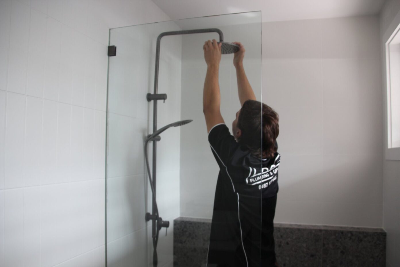Gold Coast plumbing specialist checking for showerhead leak in modern bathroom.