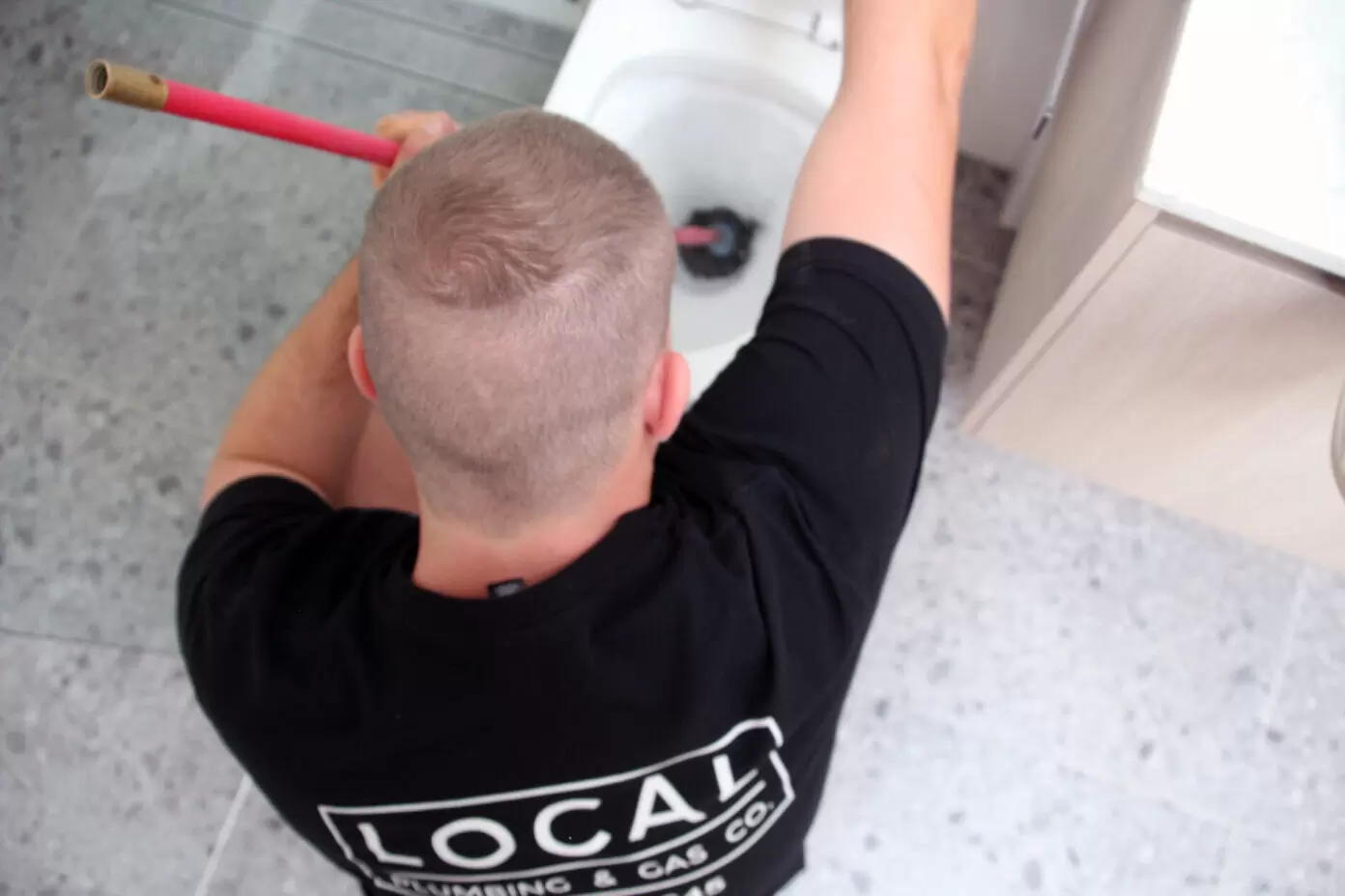 Licensed residential plumber unblocking a toilet with a manual drain rod.