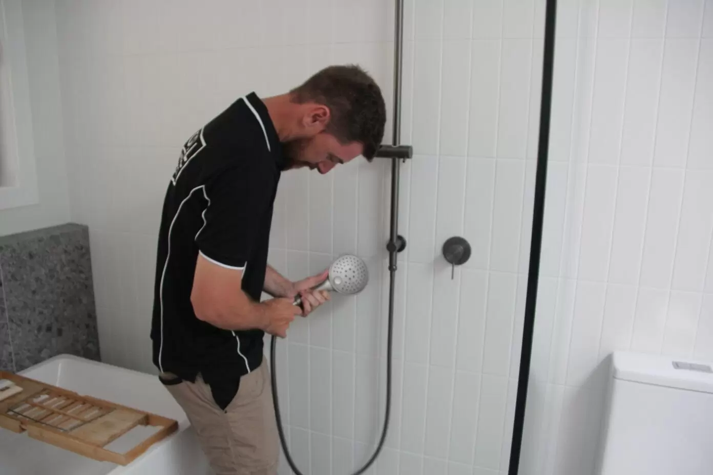 Plumber replacing leaking handheld shower hose in a Gold Coast home.