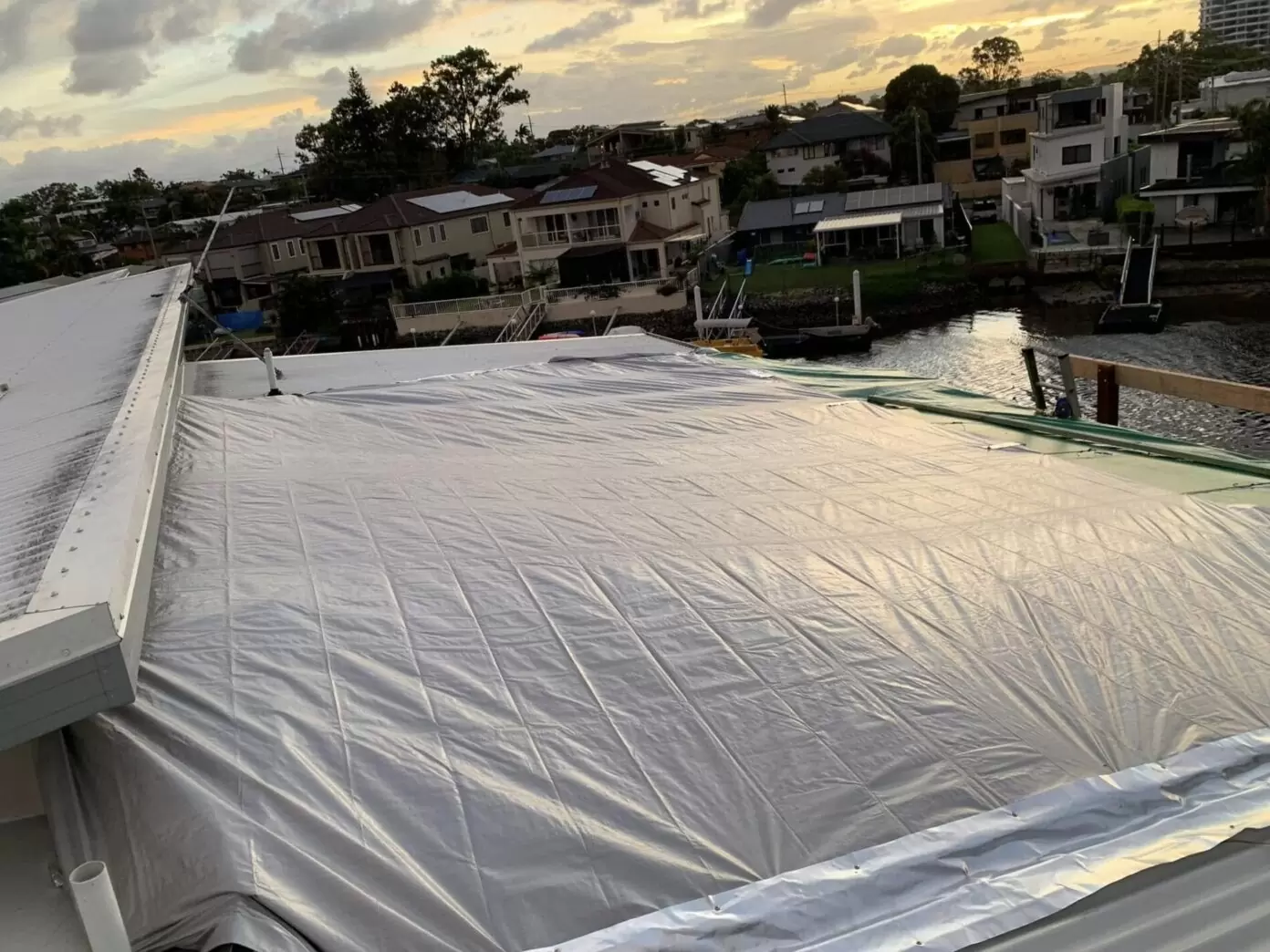 Waterfront home with a metal roof covered by a protective tarp after storm damage, showcasing temporary leak prevention measures.