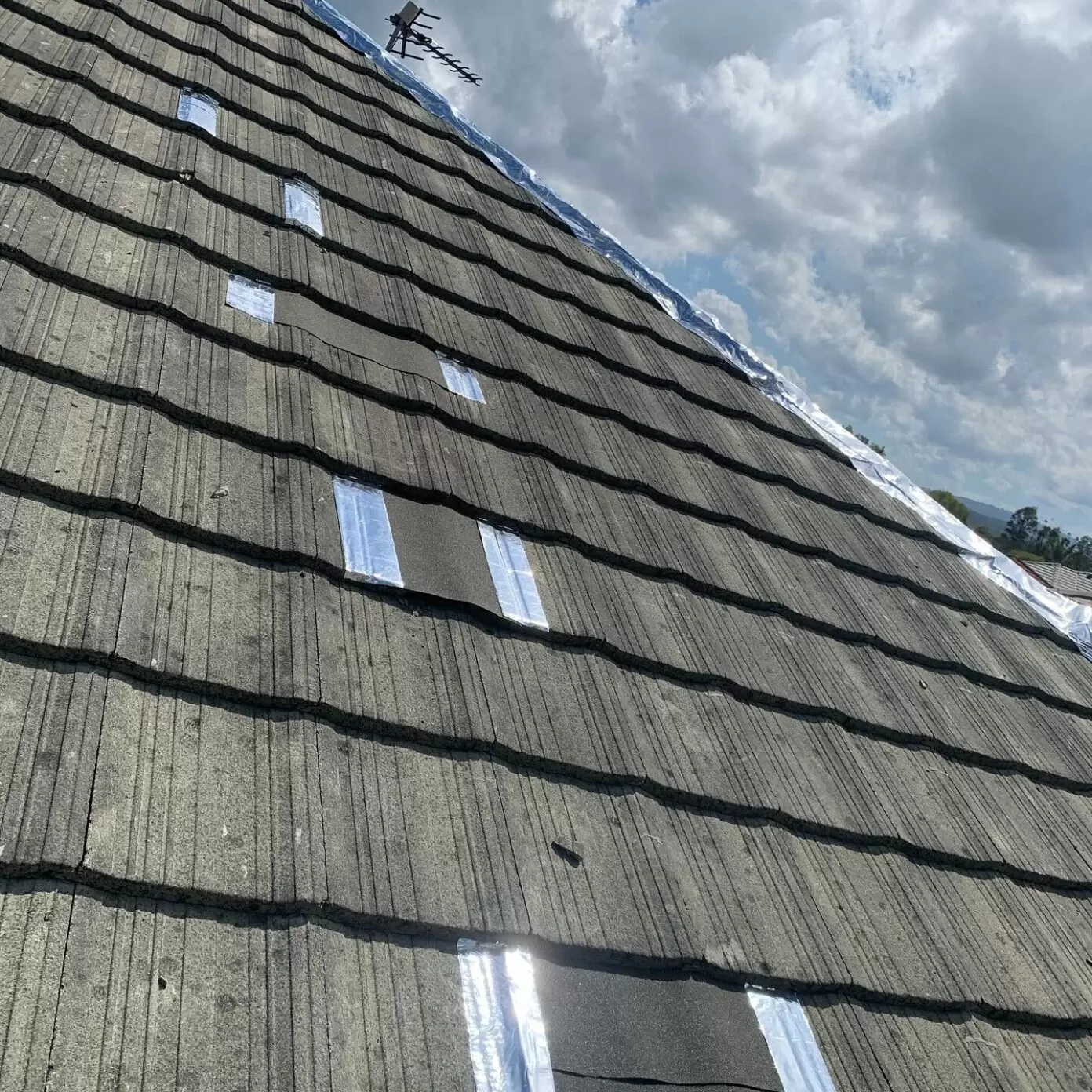 Detailed view of a tiled roof showing multiple patch repairs with flashing tape, sealing leaks and damage on a sloped residential roof.