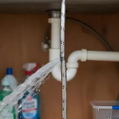Burst braided flexi hose spraying water under a kitchen sink