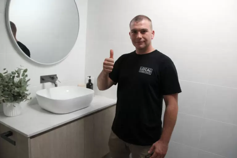 Plumber giving thumbs up beside bathroom vanity basin during bathroom plumbing service on the Gold Coast