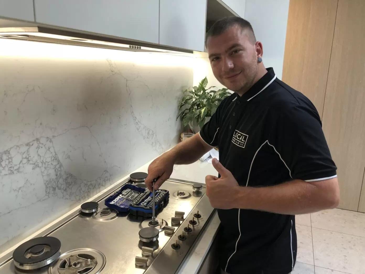 Plumber installing and adjusting gas cooktop in a modern kitchen on the Gold Coast