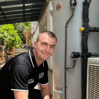 Licensed plumber working on a Rheem electric hot water system installation at a Gold Coast home