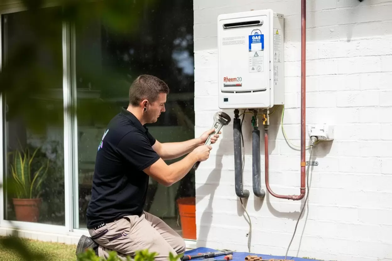 Plumber installing a Rheem instantaneous gas hot water system on an exterior wall
