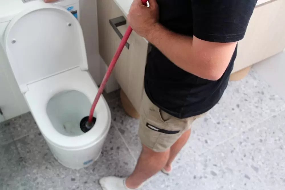 Plumber using a plunger to unblock a toilet in a bathroom