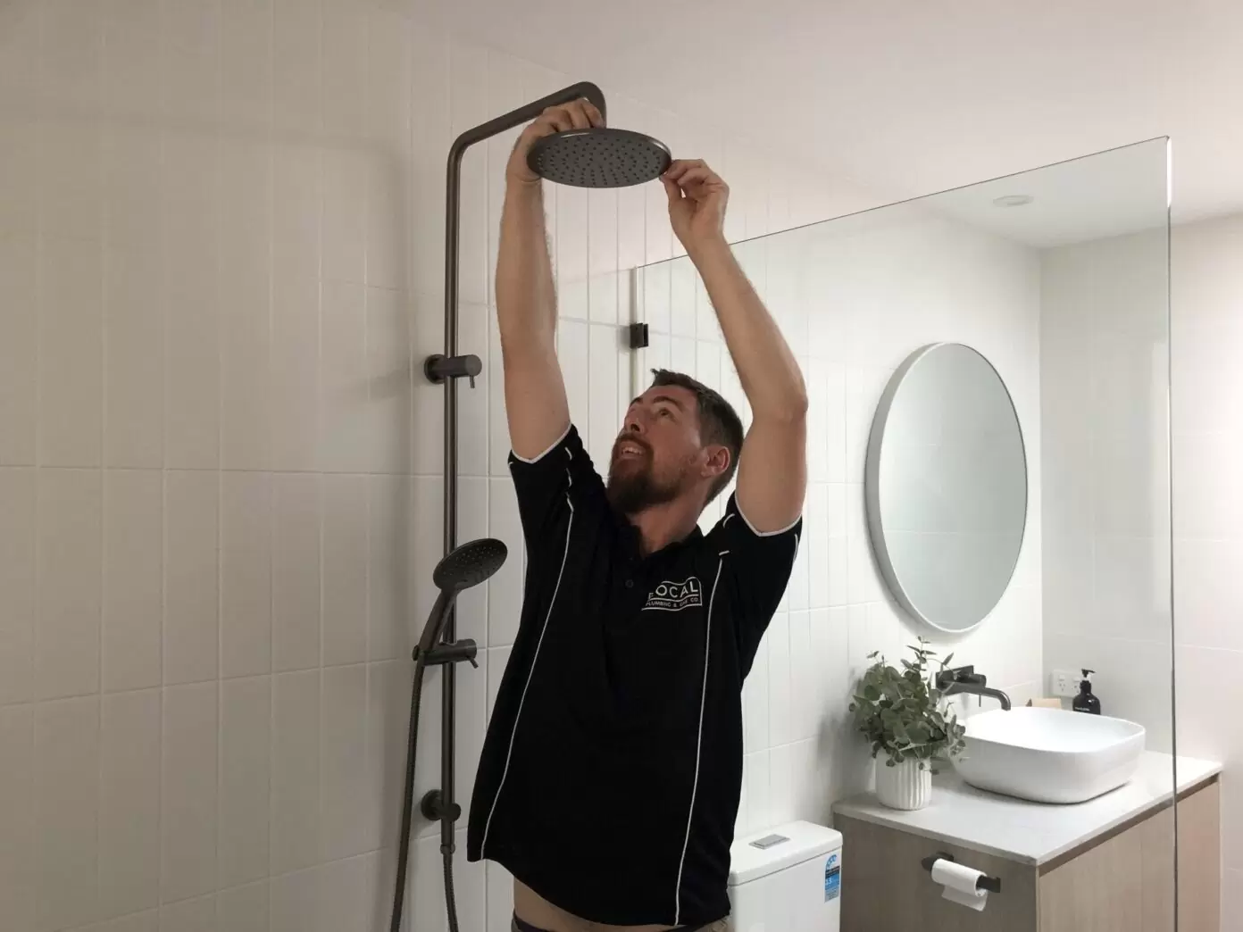 Plumber installing rainfall shower head during bathroom plumbing installation on the Gold Coast
