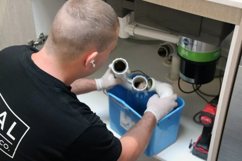 Plumber repairing under sink pipes and drainage connections in kitchen cabinet