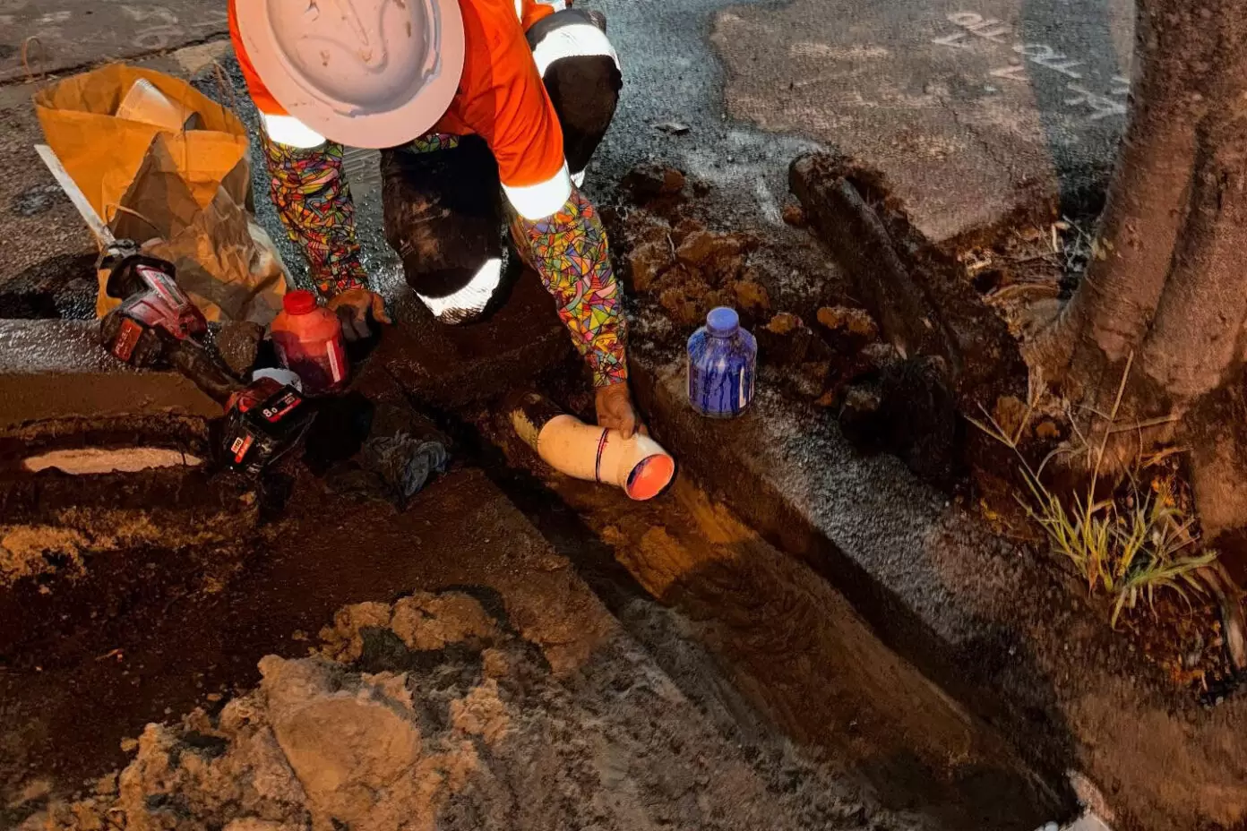 Worker installing a water main pipe during roadside excavation