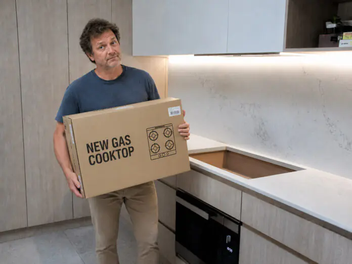 Homeowner holding new gas cooktop, asking the question, Can I Install A Gas Cooktop Myself?