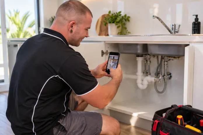 Plumber photographing a completed under-sink repair at a rental property for the property manager
